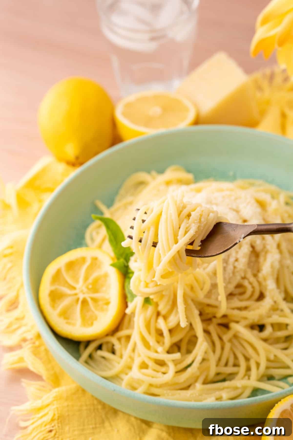 A fork pulling a bite of tiktok lemon pasta out of a mint green bowl, highlighting the perfectly coated spaghetti.
