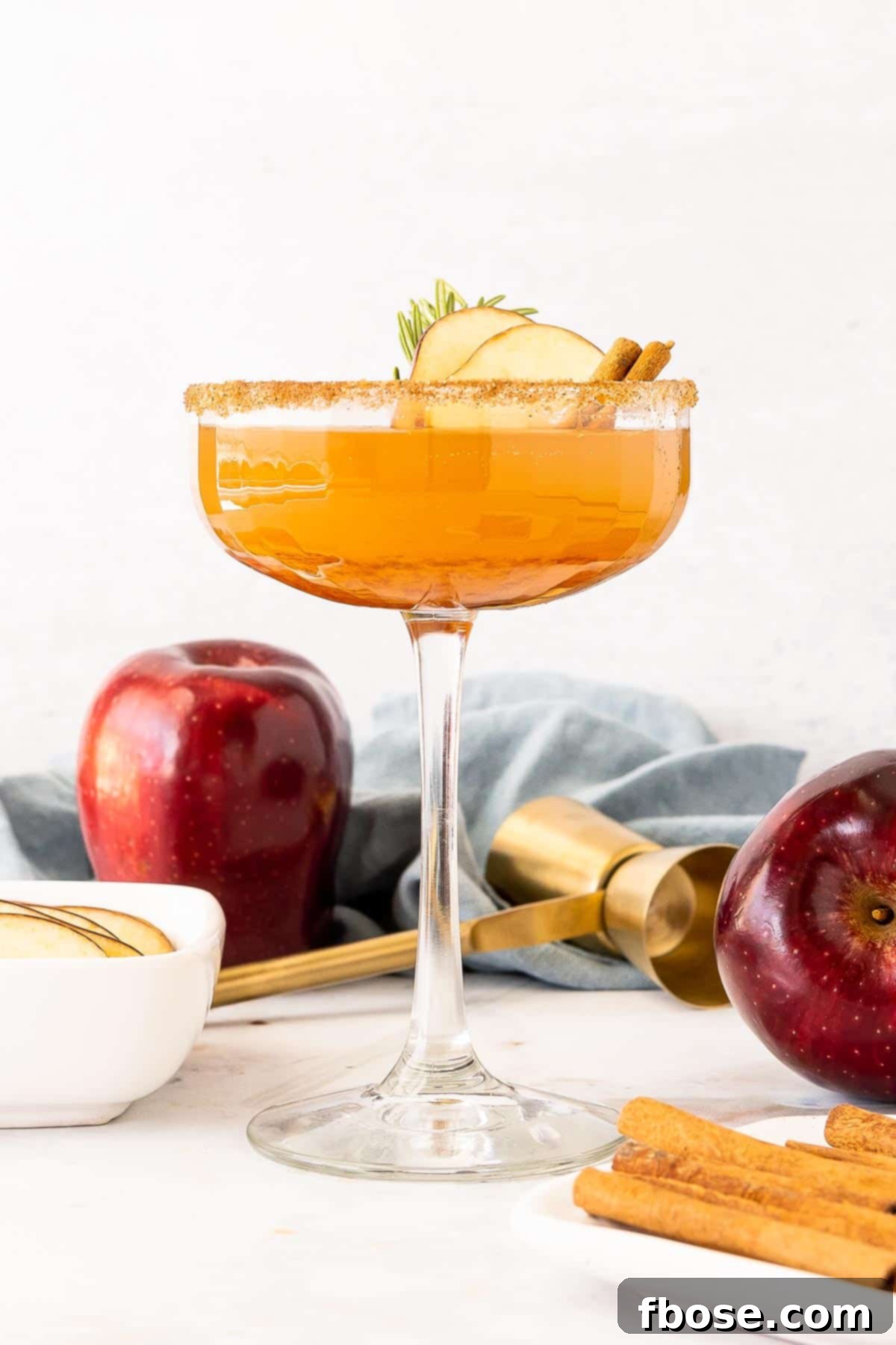 Fireside Apple Bourbon Elixir 6 A single coupe glass filled with an Apple Cider Bourbon Cocktail, garnished with an apple slice and rosemary, on a pristine white marble surface.