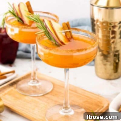Fireside Apple Bourbon Elixir 7 Two coupe glasses filled with an apple cider bourbon cocktail on a cutting board.