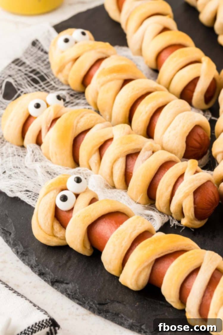 Mummy hot dogs on a black plate, showcasing their festive Halloween appeal.
