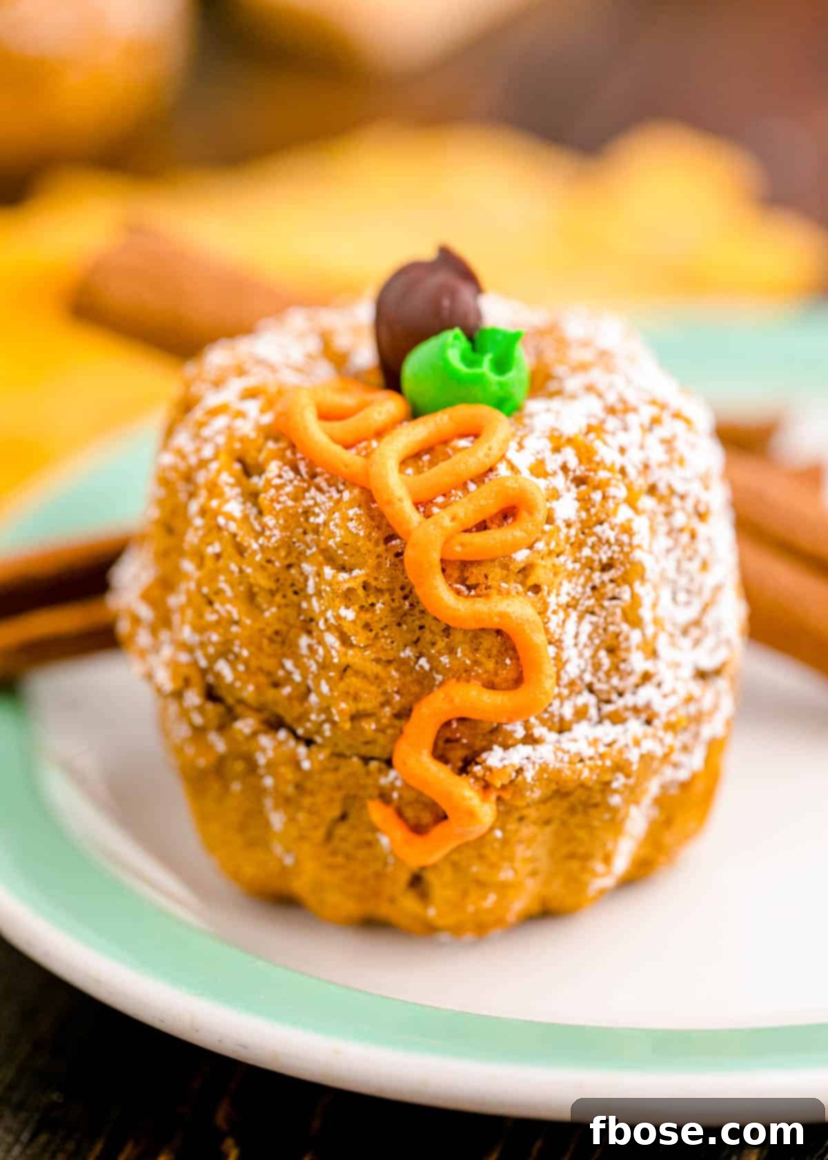 A single mini pumpkin bundt cake, perfectly frosted and decorated, sits on an elegant white and mint green plate, ready to be enjoyed.
