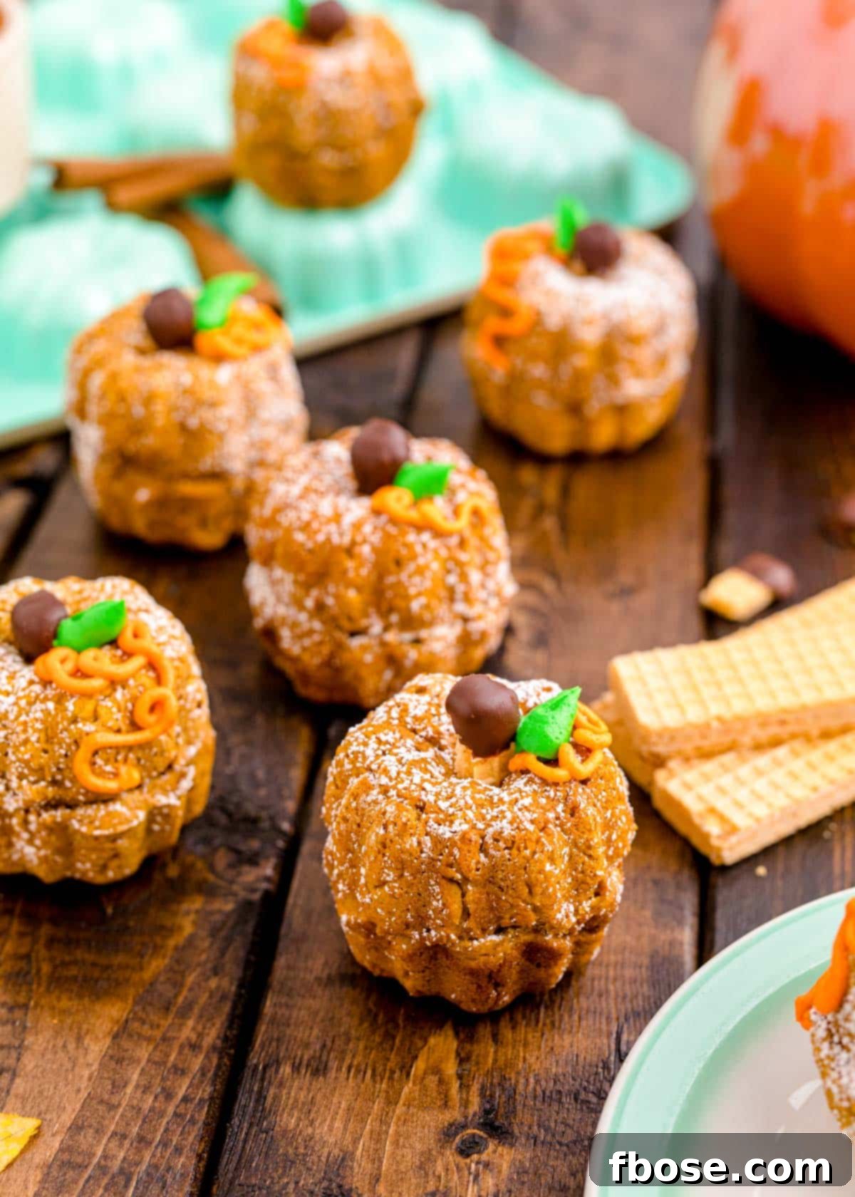 A beautiful arrangement of freshly baked mini pumpkin bundt cakes, some adorned with frosting, resting on a rustic wooden table, showcasing their golden-brown color and intricate bundt design.