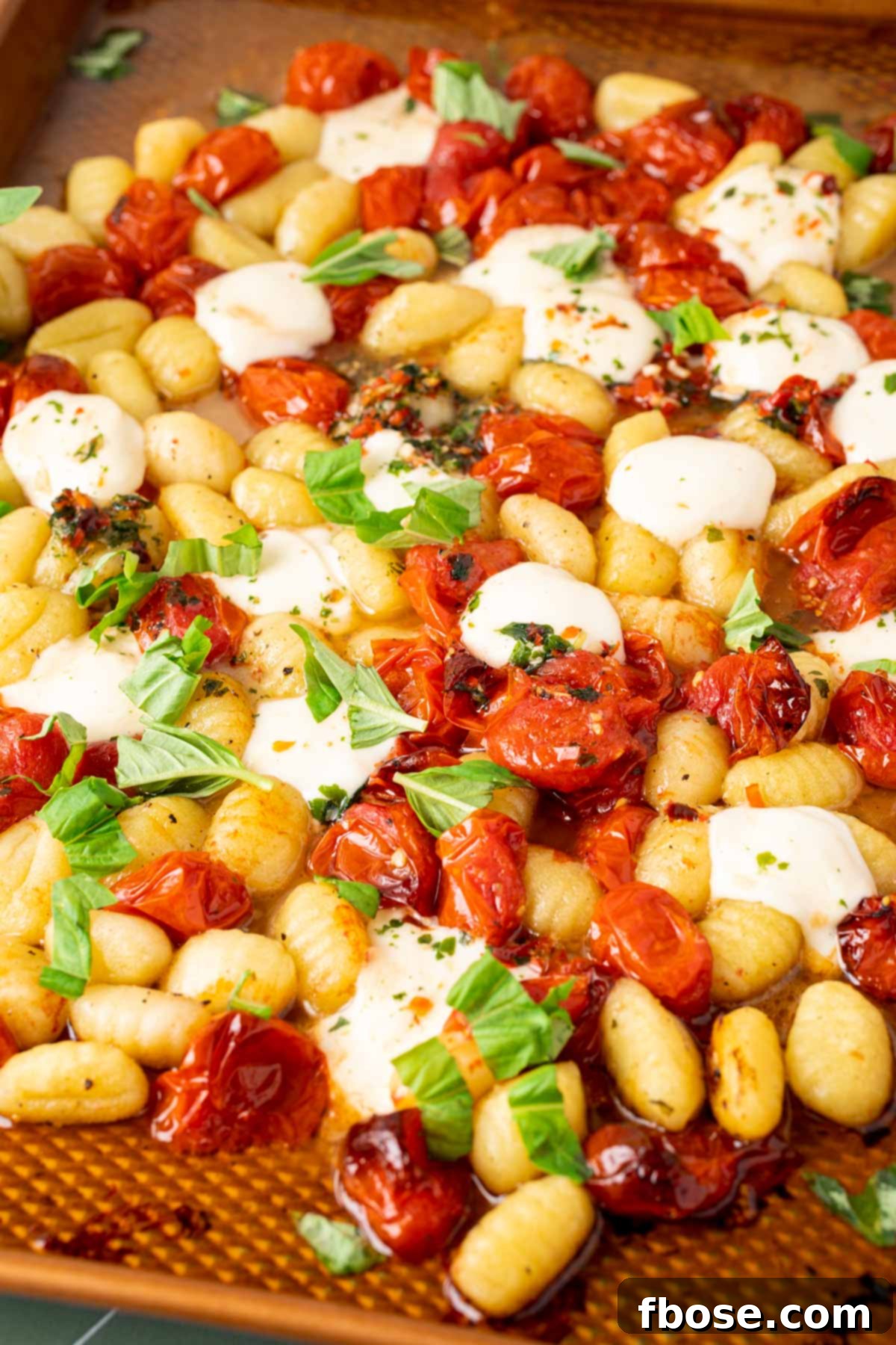 A vibrant sheet pan of baked gnocchi with blistered cherry tomatoes and melted mozzarella, fresh out of the oven.