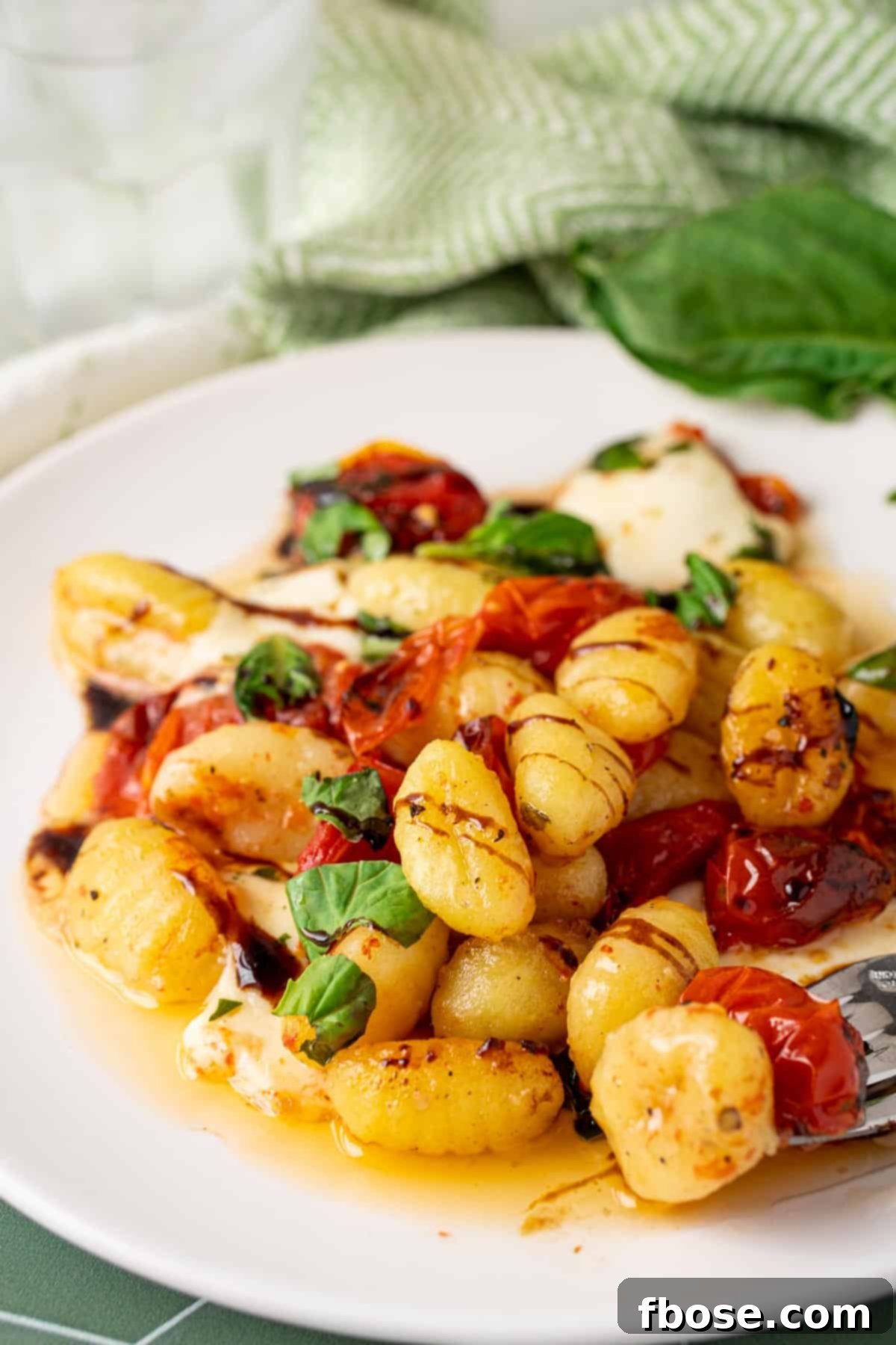 A close-up of baked Caprese gnocchi on a white plate, garnished with fresh basil.