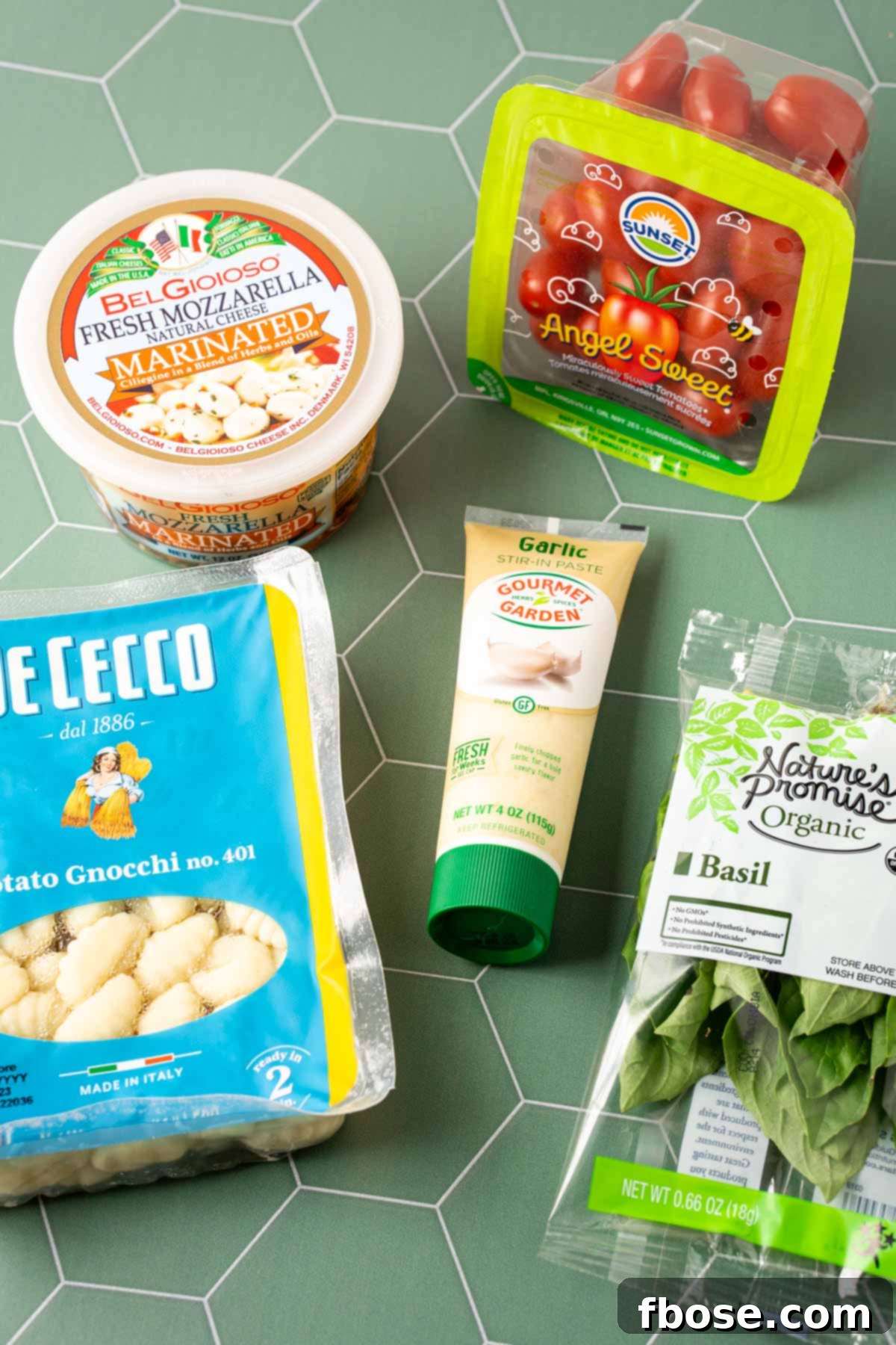 Ingredients laid out on a green surface for TikTok baked gnocchi, including gnocchi, tomatoes, mozzarella, and garlic paste.