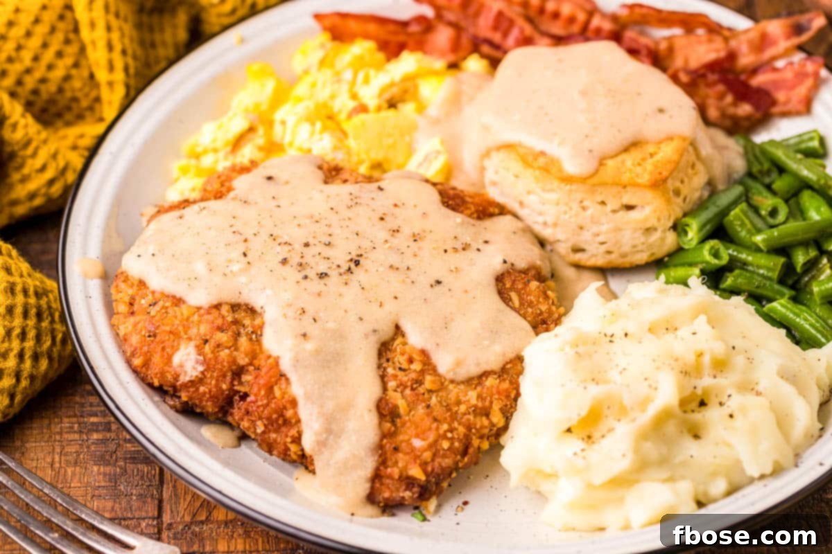 Country friend steak on a white plate with mashed potatoes, eggs, bacon, and a biscuit.