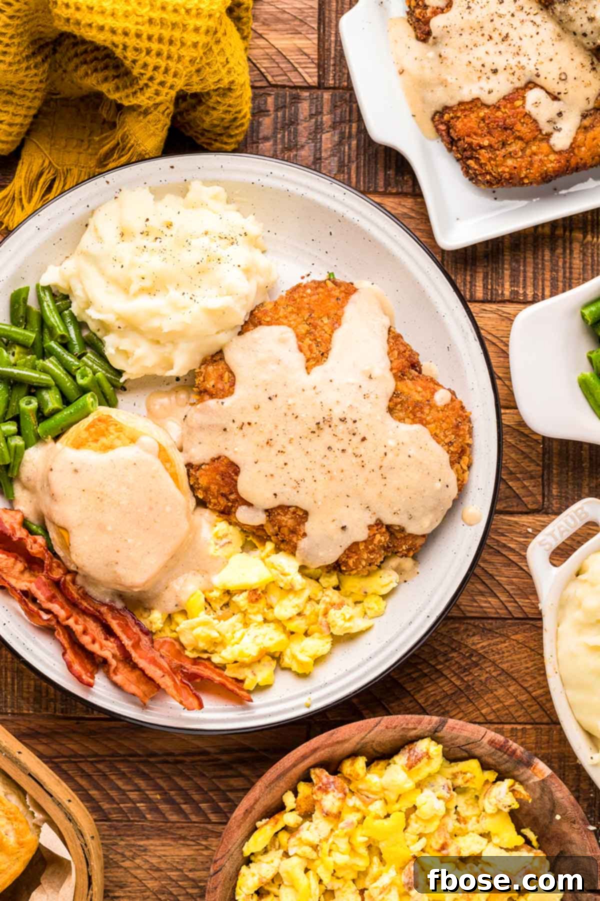 Overhead photo of a plate of country fried steak, bacon, eggs, and biscuits on a wooden table.