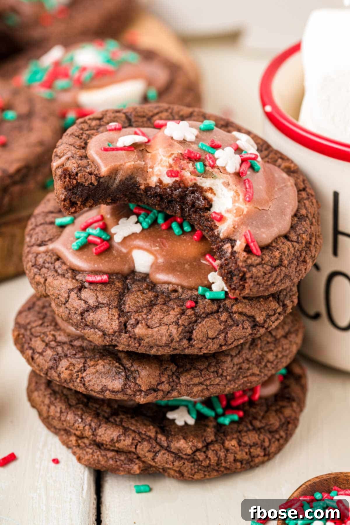 A stack of hot chocolate cookies next to a mug, showcasing their rich chocolate color and marshmallow topping.