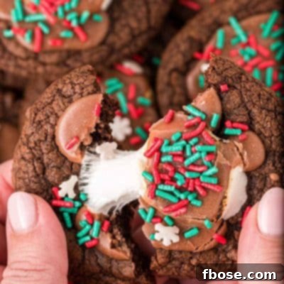 A woman's hand pulling a hot chocolate cookie apart, revealing the gooey marshmallow and fudgy interior.