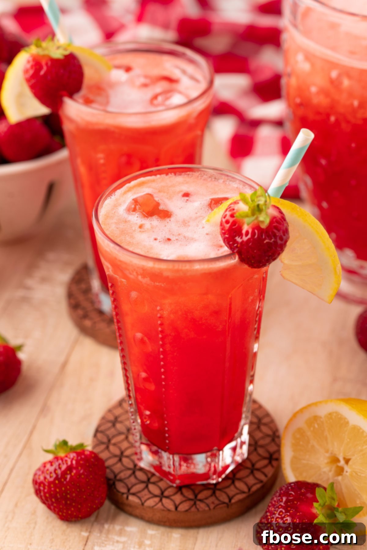 Two glasses of sparkling strawberry lemonade on rustic wooden coasters, set on a warm wooden table, capturing the essence of a refreshing summer drink.