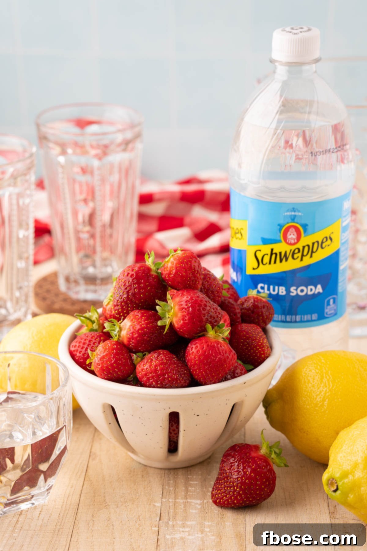 A vibrant collection of ingredients for homemade strawberry lemonade, including fresh strawberries, whole lemons, and a clear glass jar of simple syrup, neatly arranged on a rustic wooden table.