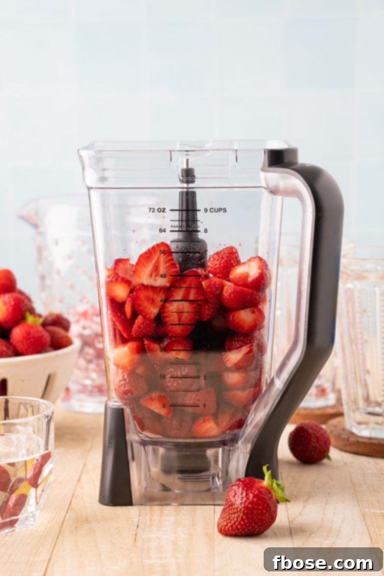 Freshly washed and halved strawberries, ready to be blended, inside a blender jar, highlighting the natural color of the fruit.