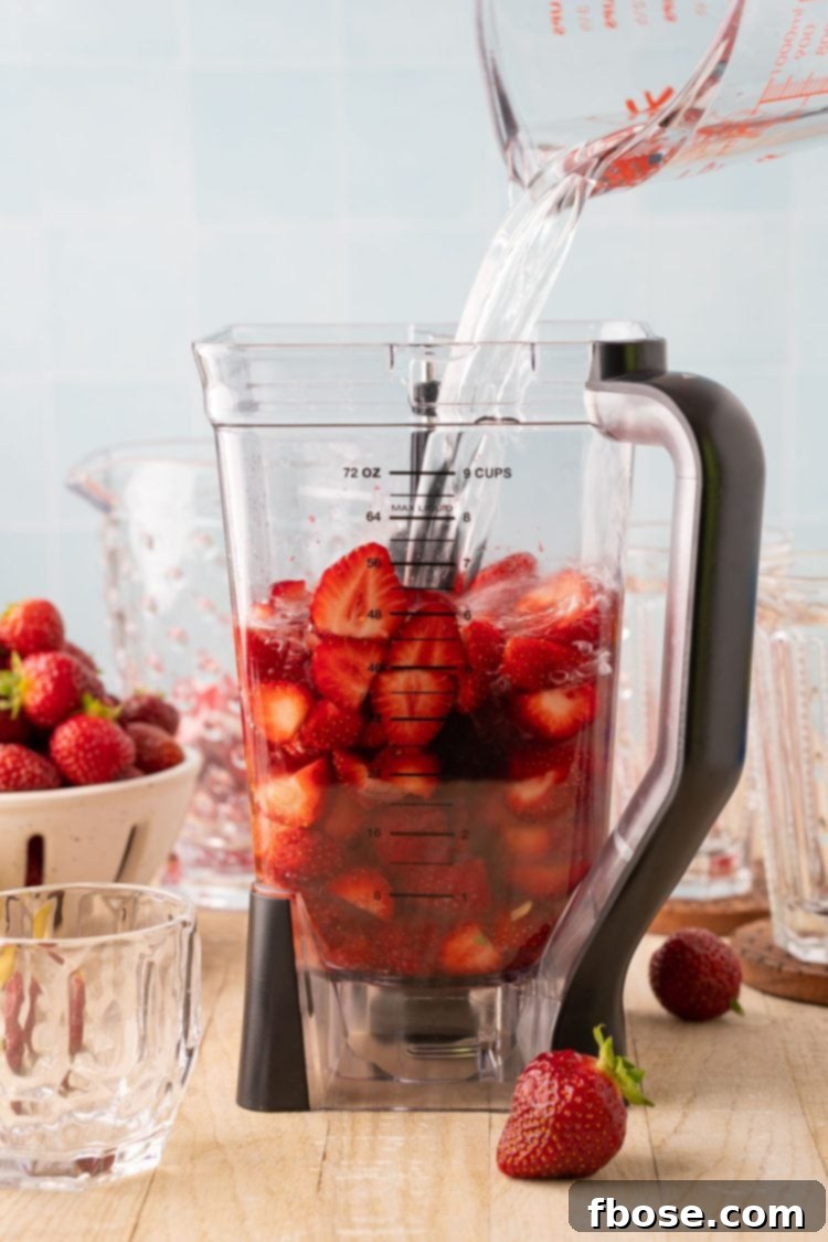 Water being poured into a blender containing strawberries, freshly squeezed lemon juice, and simple syrup, ready for blending into a concentrate.