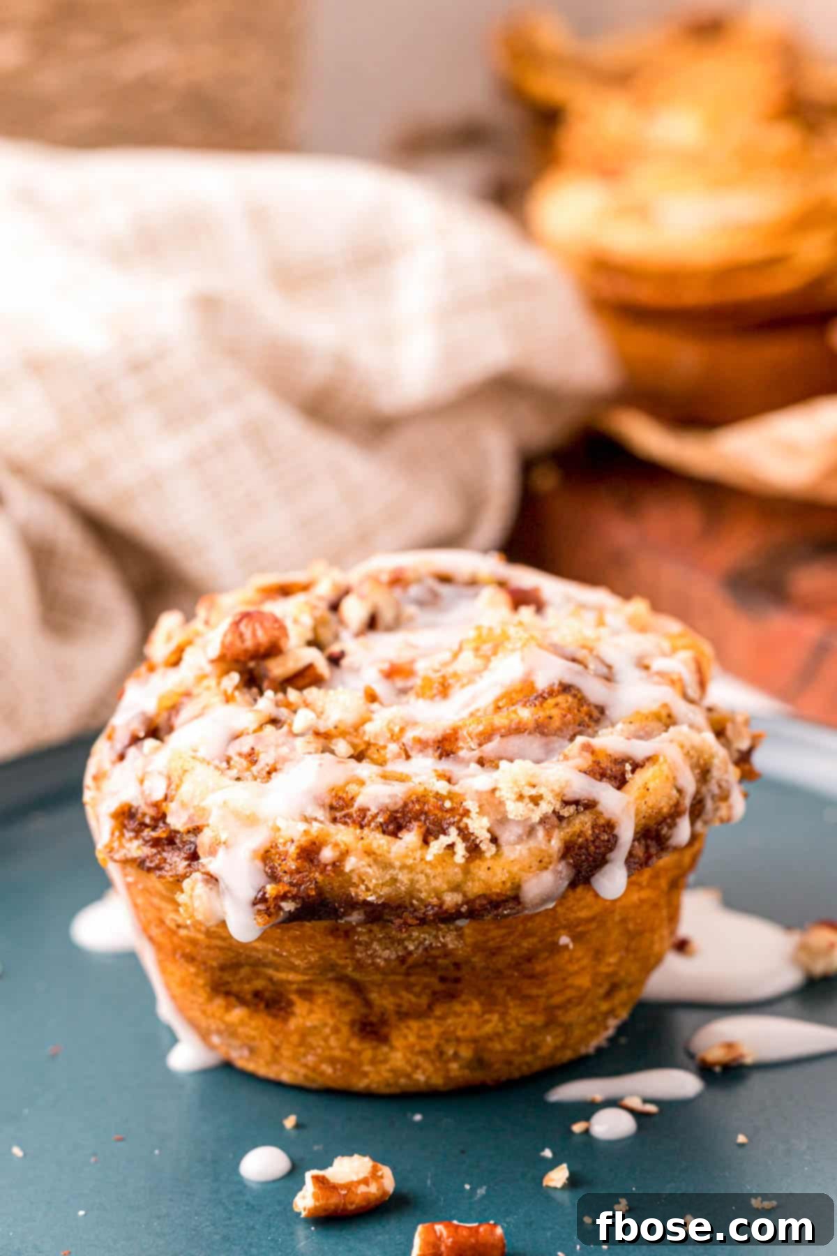 A single Pumpkin Cinnamon Roll Muffin with white glaze on a rustic blue plate.