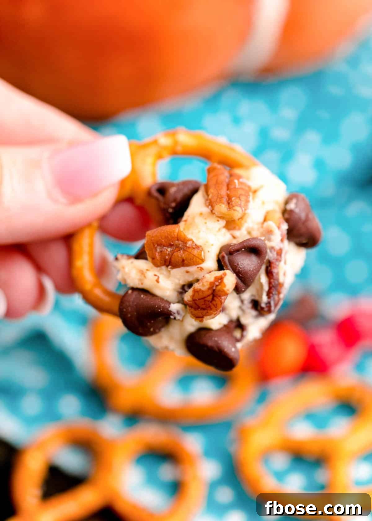 A woman's hand gracefully holding a pretzel adorned with a generous scoop of the festive dessert cheeseball.