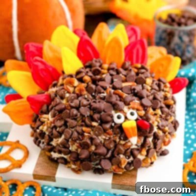 A dessert cheeseball decorated like a turkey on a white and wood cutting board.