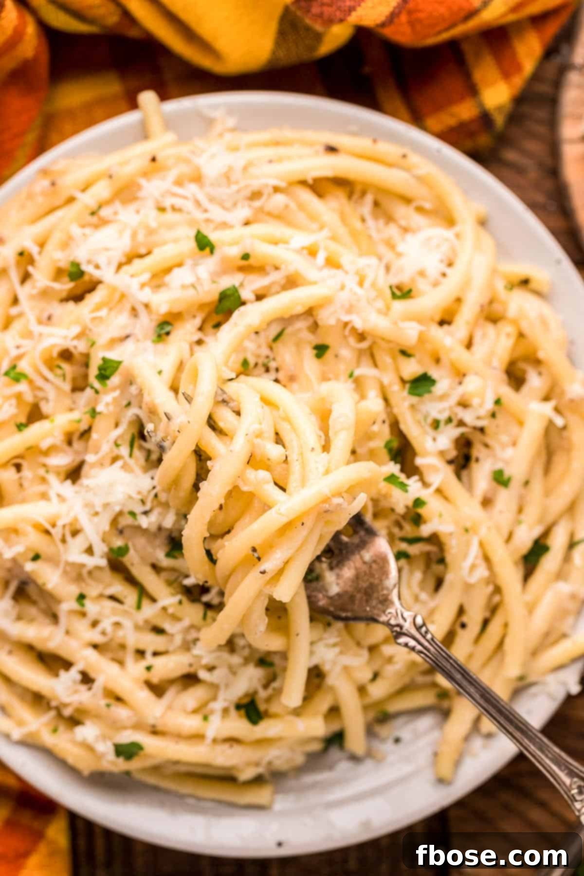 A fork elegantly twirling a generous portion of bucatini cacio e pepe on a white plate, highlighting the creamy sauce and black pepper specks.