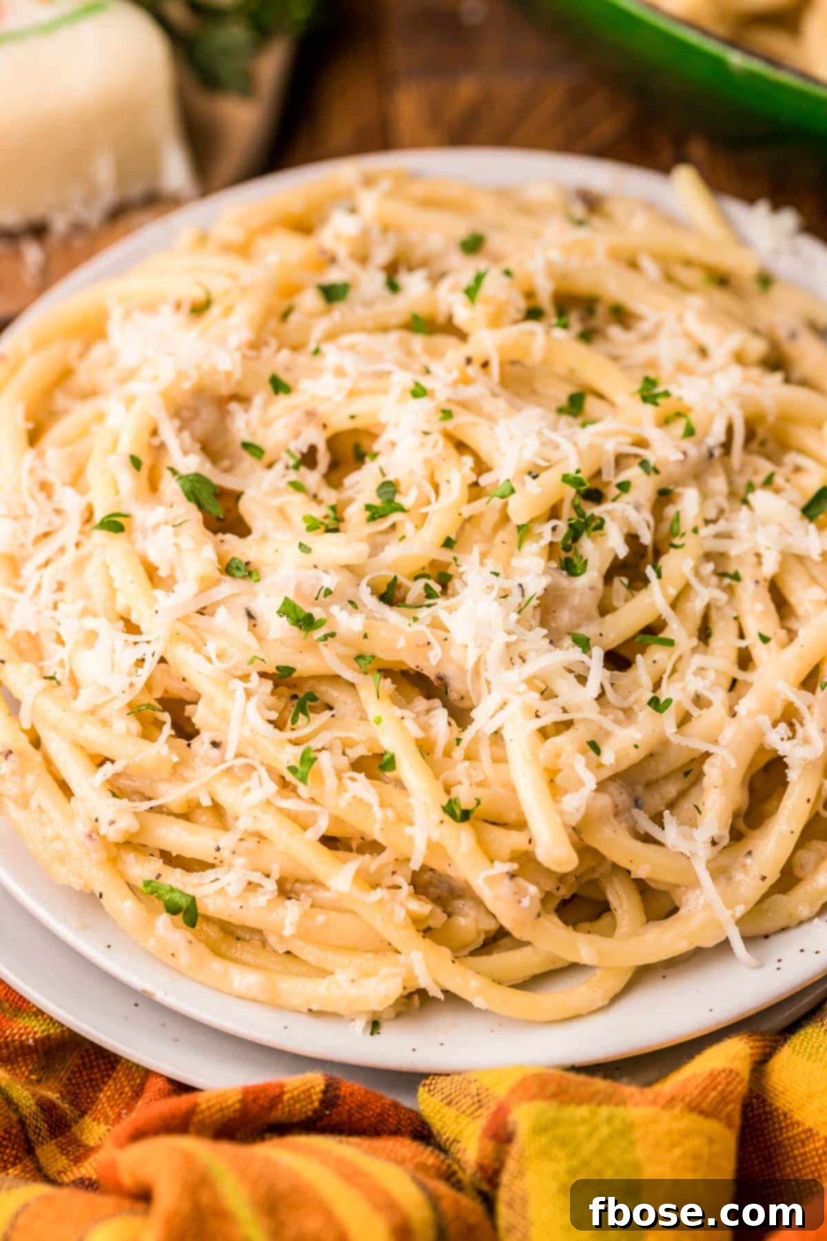 A generous serving of bucatini cacio e pepe in a serving bowl, garnished with fresh basil leaves and extra black pepper.