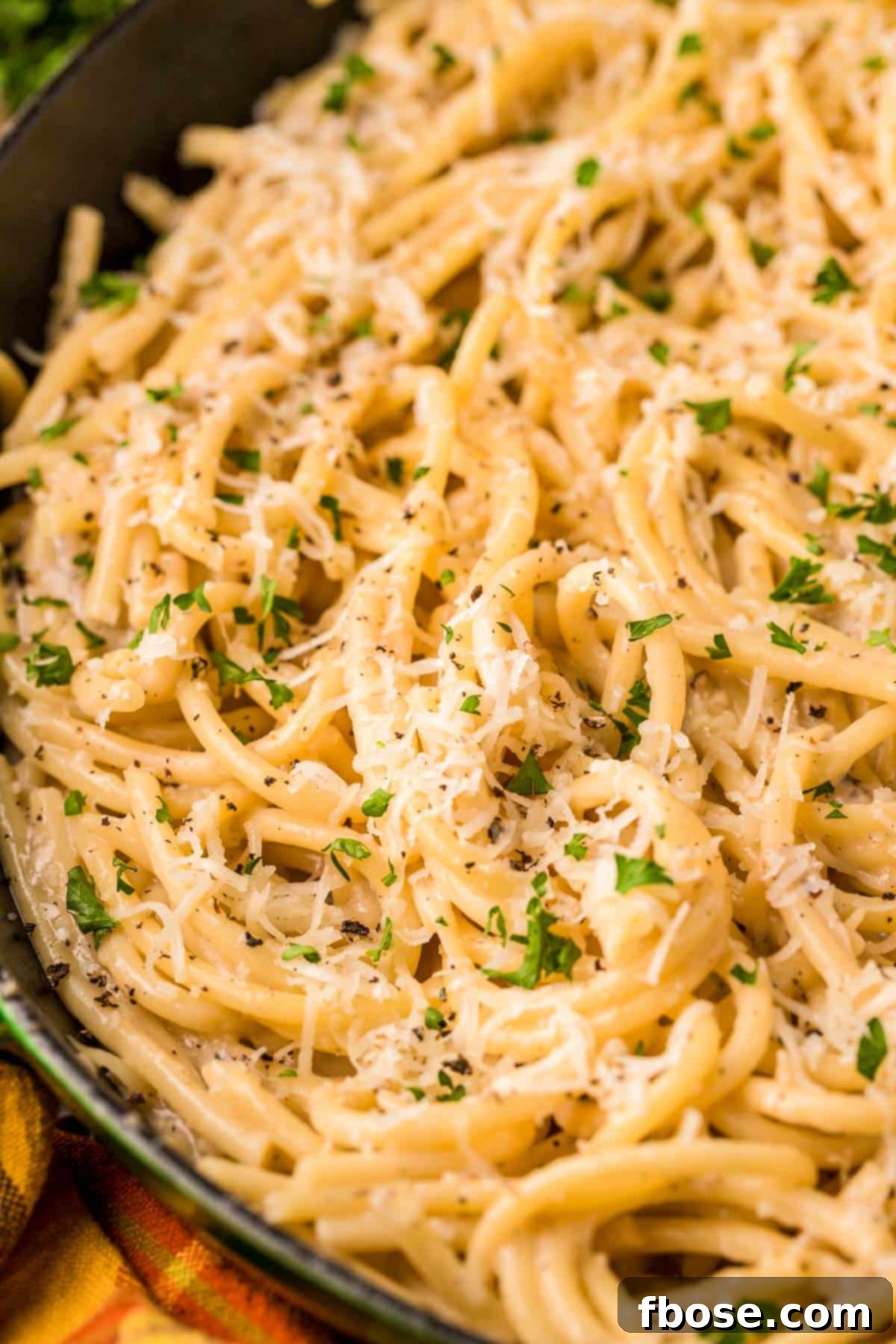 Close-up of bucatini cacio e pepe served in a rustic skillet, showing the glossy, cheesy sauce and thick pasta strands, garnished with fresh pepper.