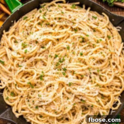Overhead photo of bucatini cacio e pepe in a green and black skillet on a wooden table.