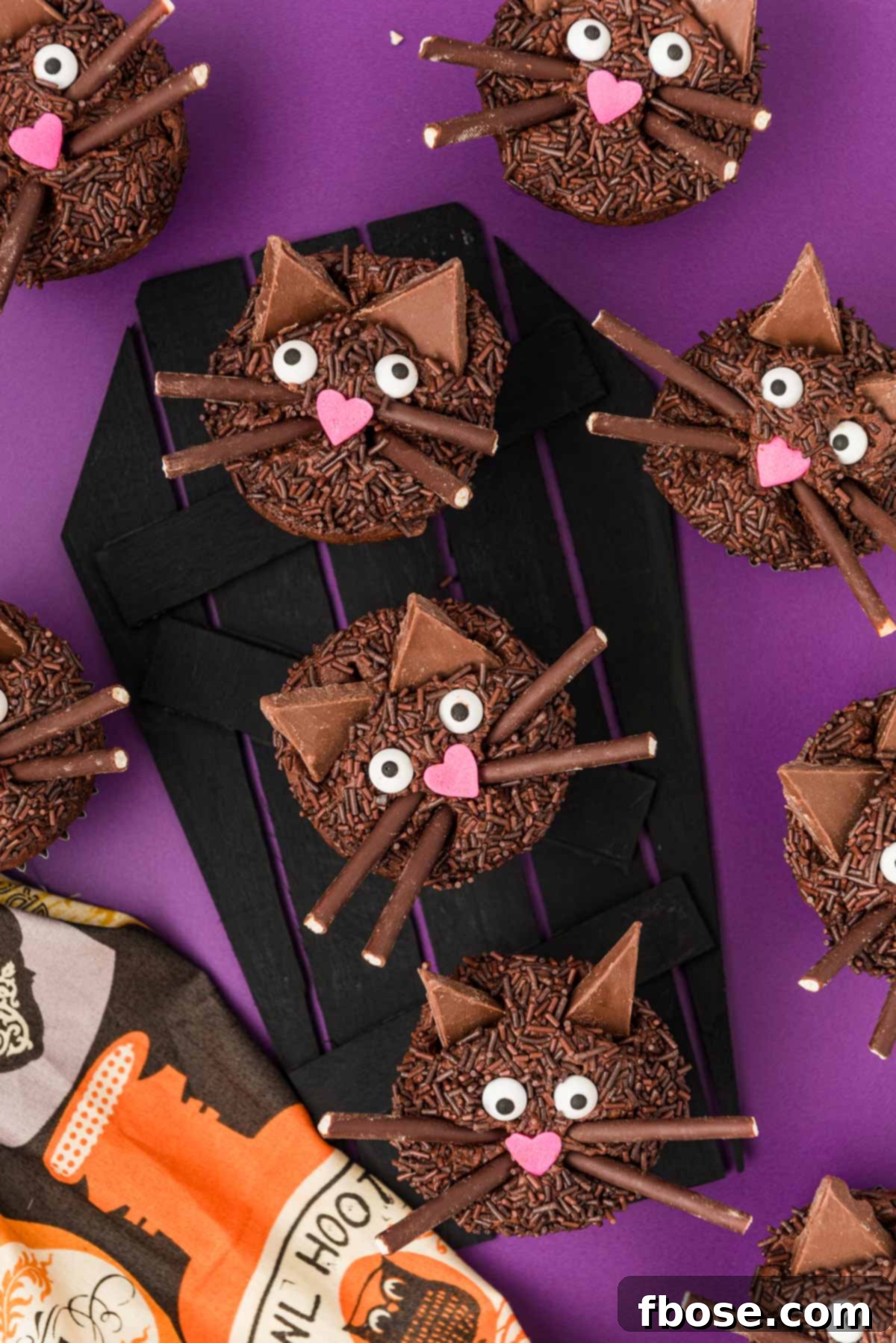 Overhead photo of black cat cupcakes on a purple surface.