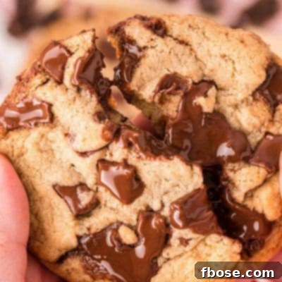 A woman's hand breaking a brown butter chocolate chip cookie in half.