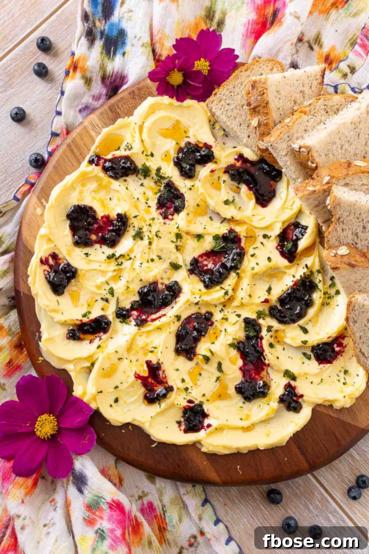 TikTok's Viral Butter Board 2 Overhead photo of a butter board on a floral napkin, showcasing Irish butter, blueberry jam, lemon zest, honey, and fresh basil.