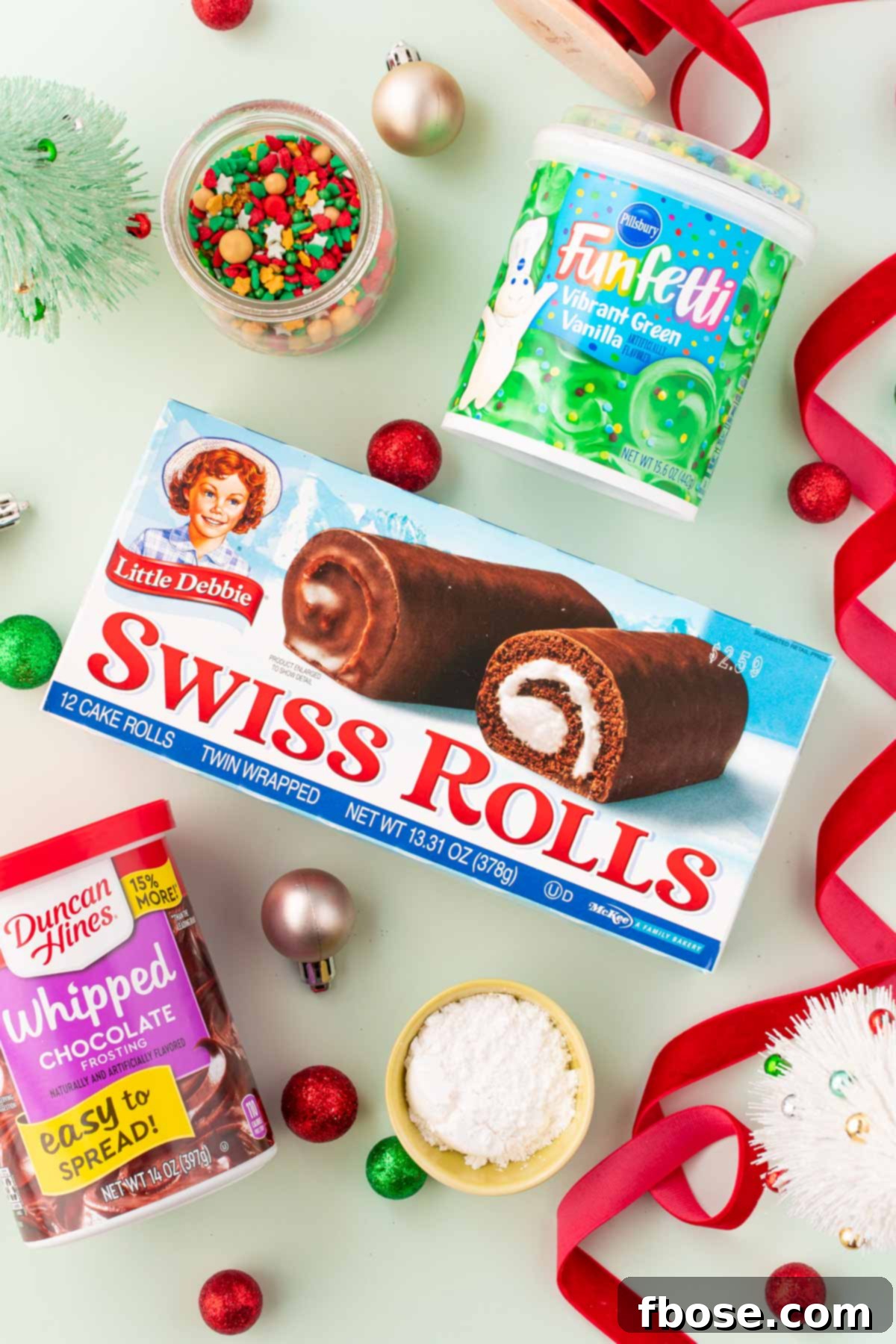 Ingredients to make mini yule logs on a green surface with holiday decor.