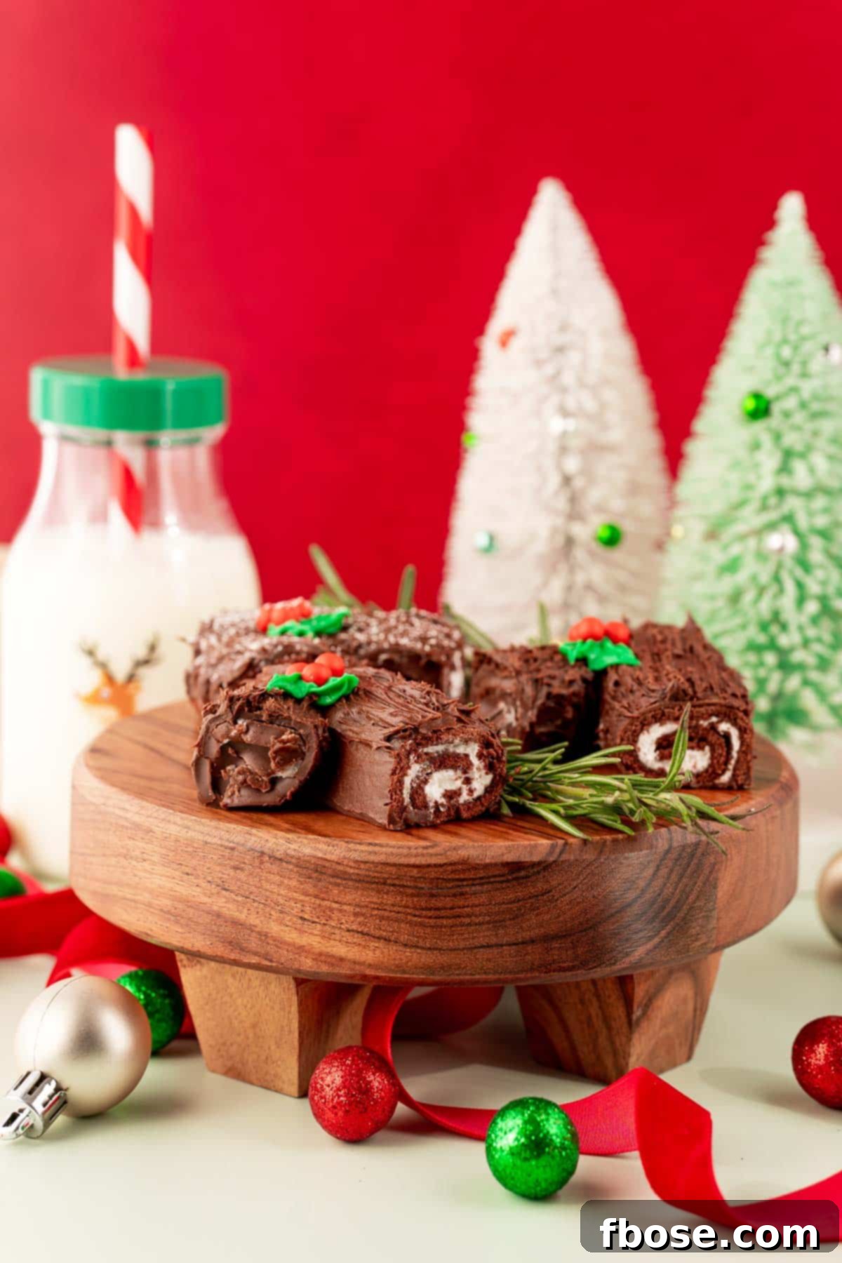 Mini yule log cakes on a cake stand with holiday decorations in the background.