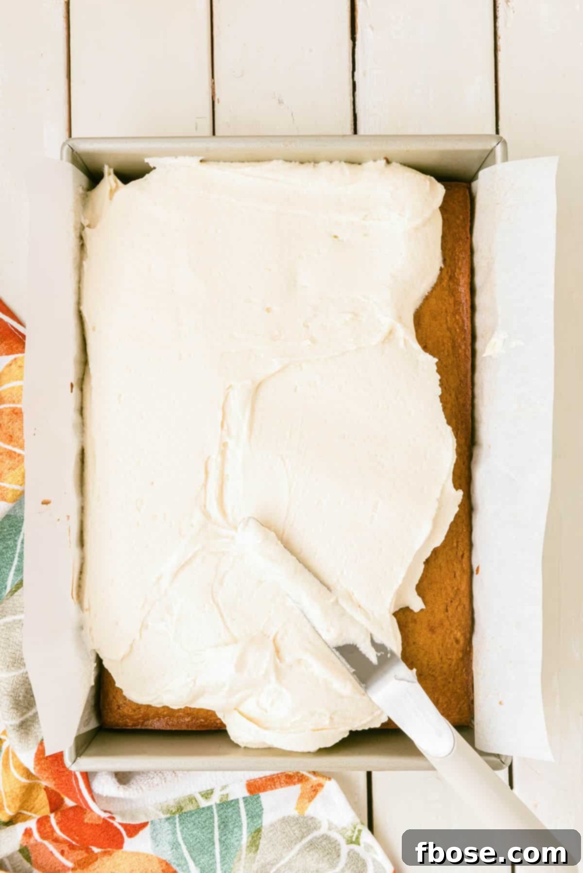 Effortless Autumn Pumpkin Bake 10 A smooth layer of cream cheese frosting being expertly spread across a perfectly baked pumpkin cake still in its pan, creating a delicious finish.