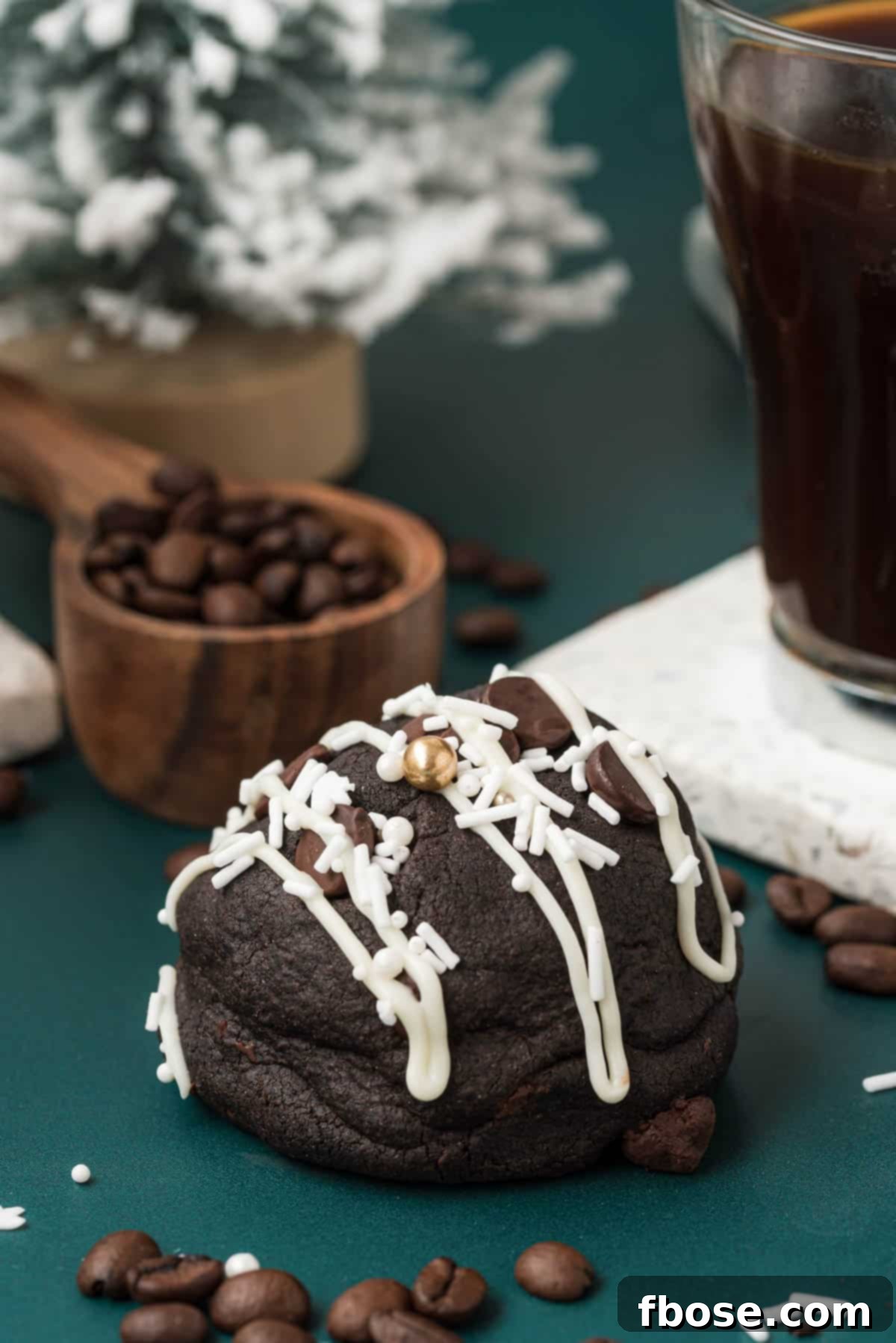 A beautifully decorated Gourmet Peppermint Mocha Cookie resting on a vibrant green surface, showcasing its festive white chocolate drizzle and sprinkles.