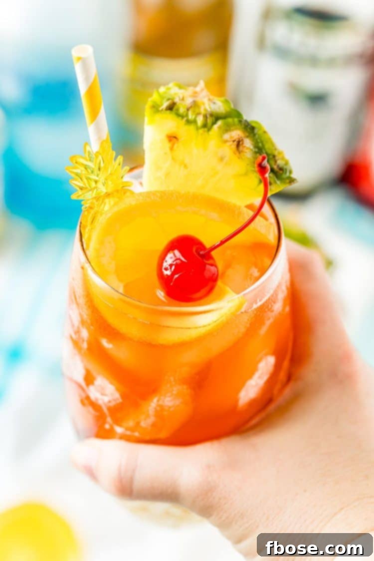 Woman's hand holding a glass filled with a rum runner cocktail garnished with orange, pineapple, and cherry.