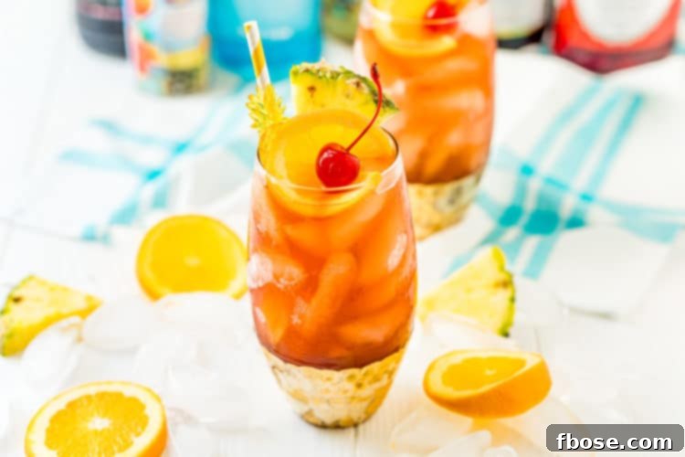 Rum Runner cocktail on a white table with slices of fruit and ice cubes scattered around it.