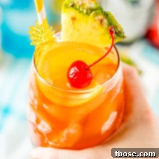 Woman's hand holding a glass filled with a rum runner cocktail garnished with orange, pineapple, and cherry.
