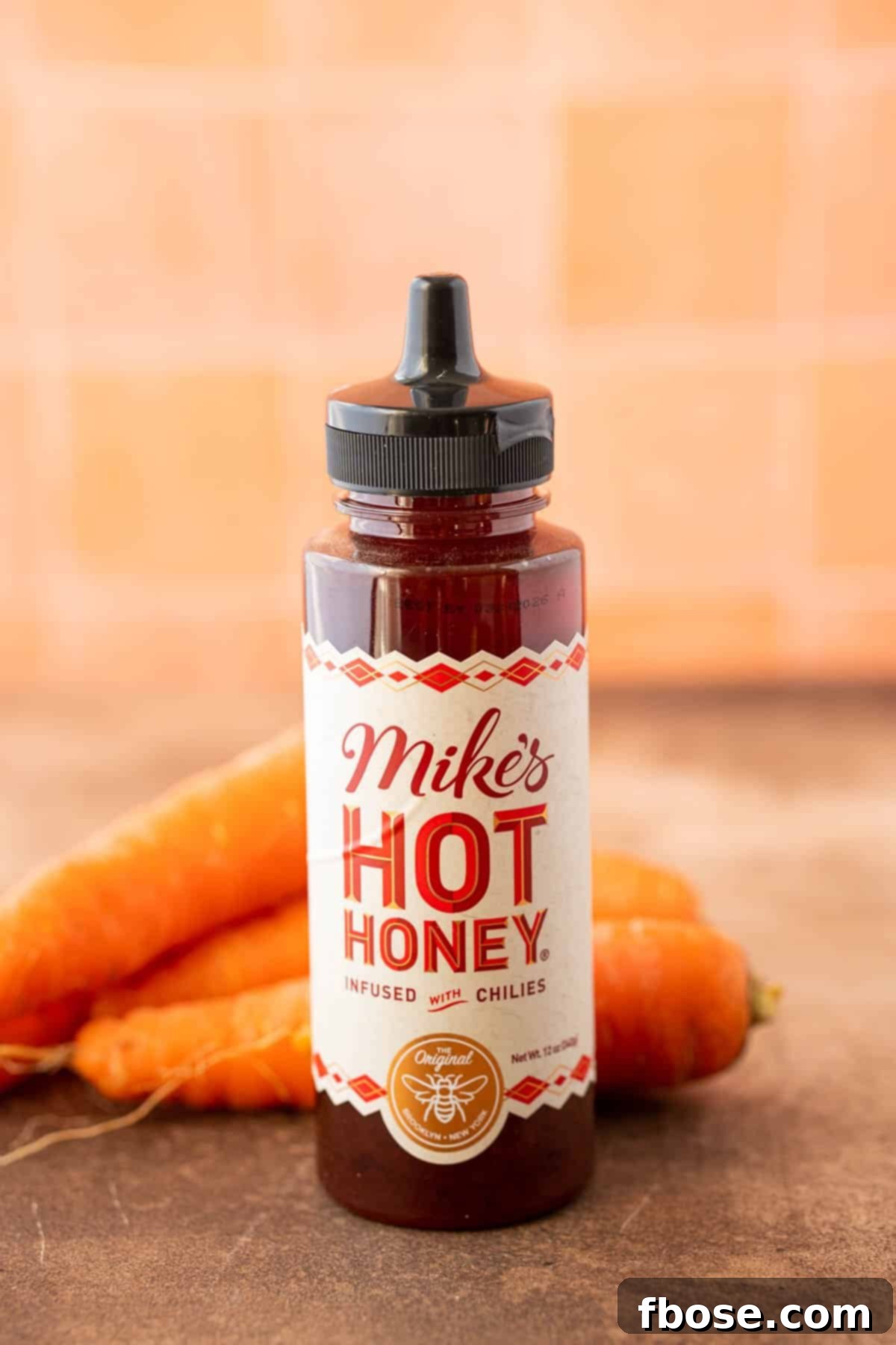 Irresistible Hot Honey Glazed Carrots 3 A bottle of hot honey on a table with carrots behind it.