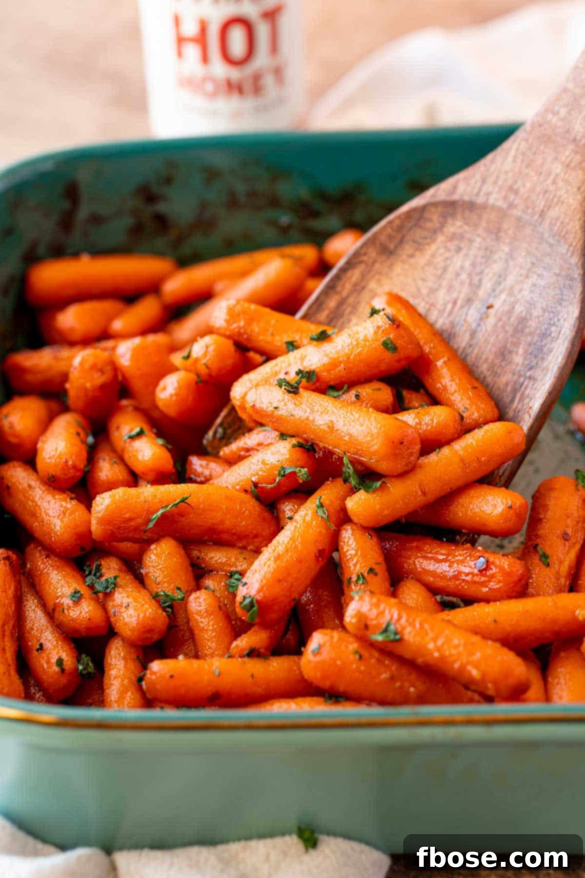 Irresistible Hot Honey Glazed Carrots 5 A serving spoon scooping hot honey glazed carrots out of a baking dish.