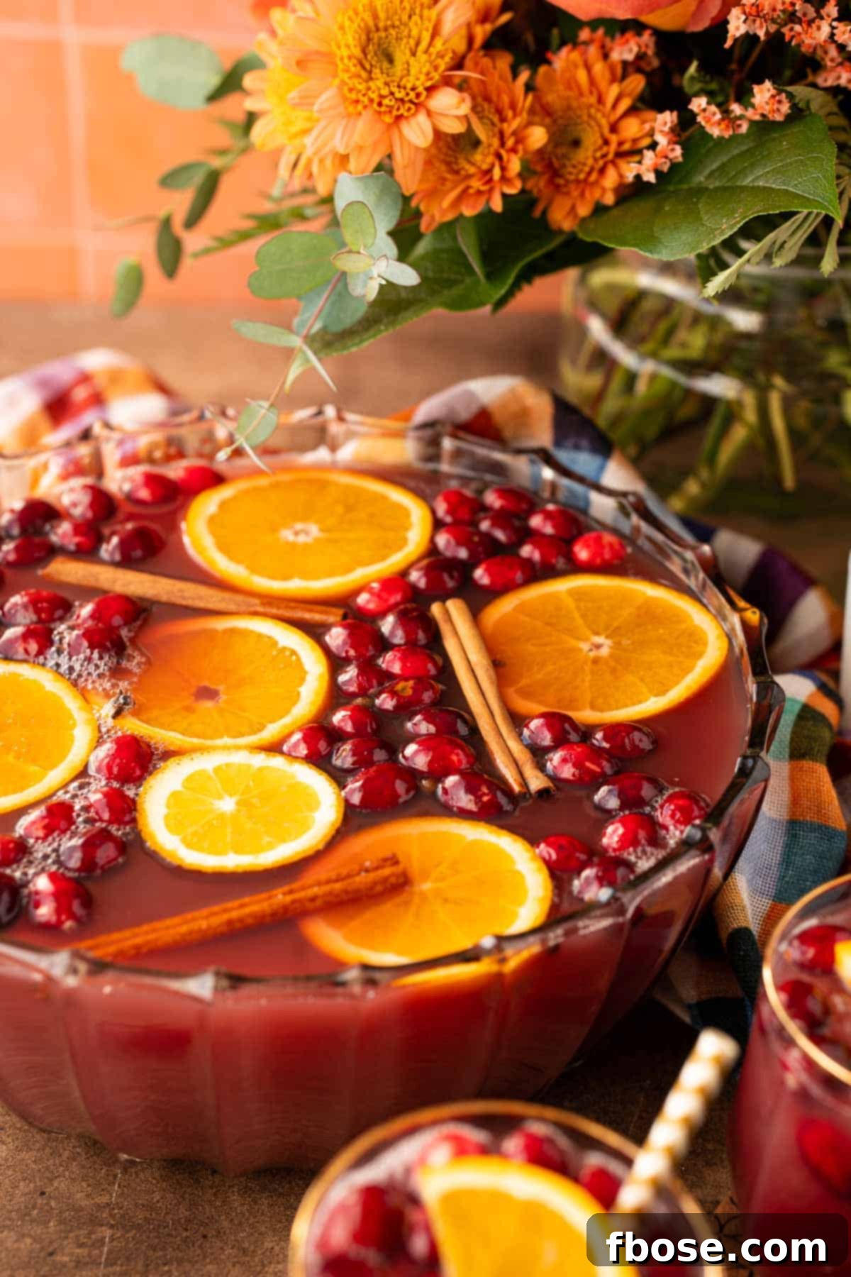 A punch bowl filled with autumn punch, garnished with orange slices and cranberries.