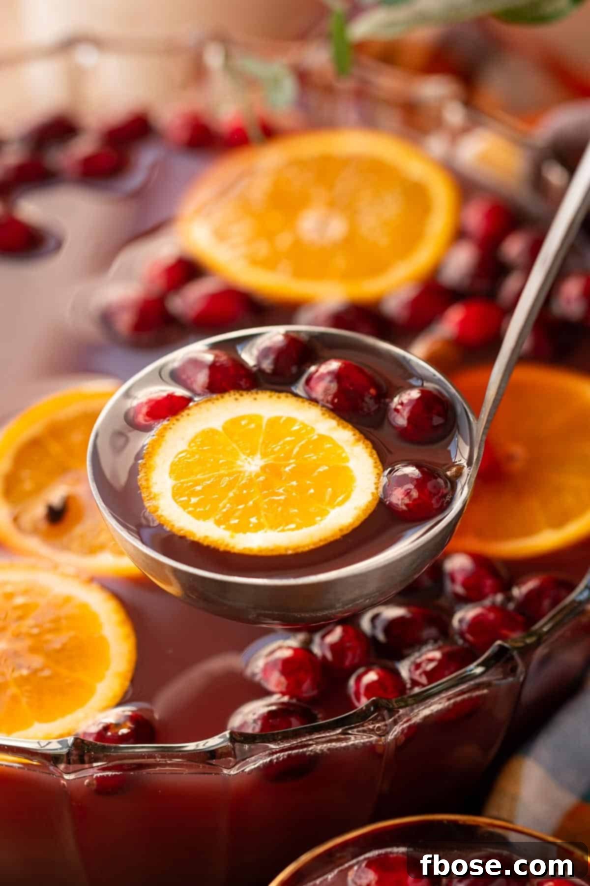 A ladle scooping autumn punch out of a punch bowl with ice.