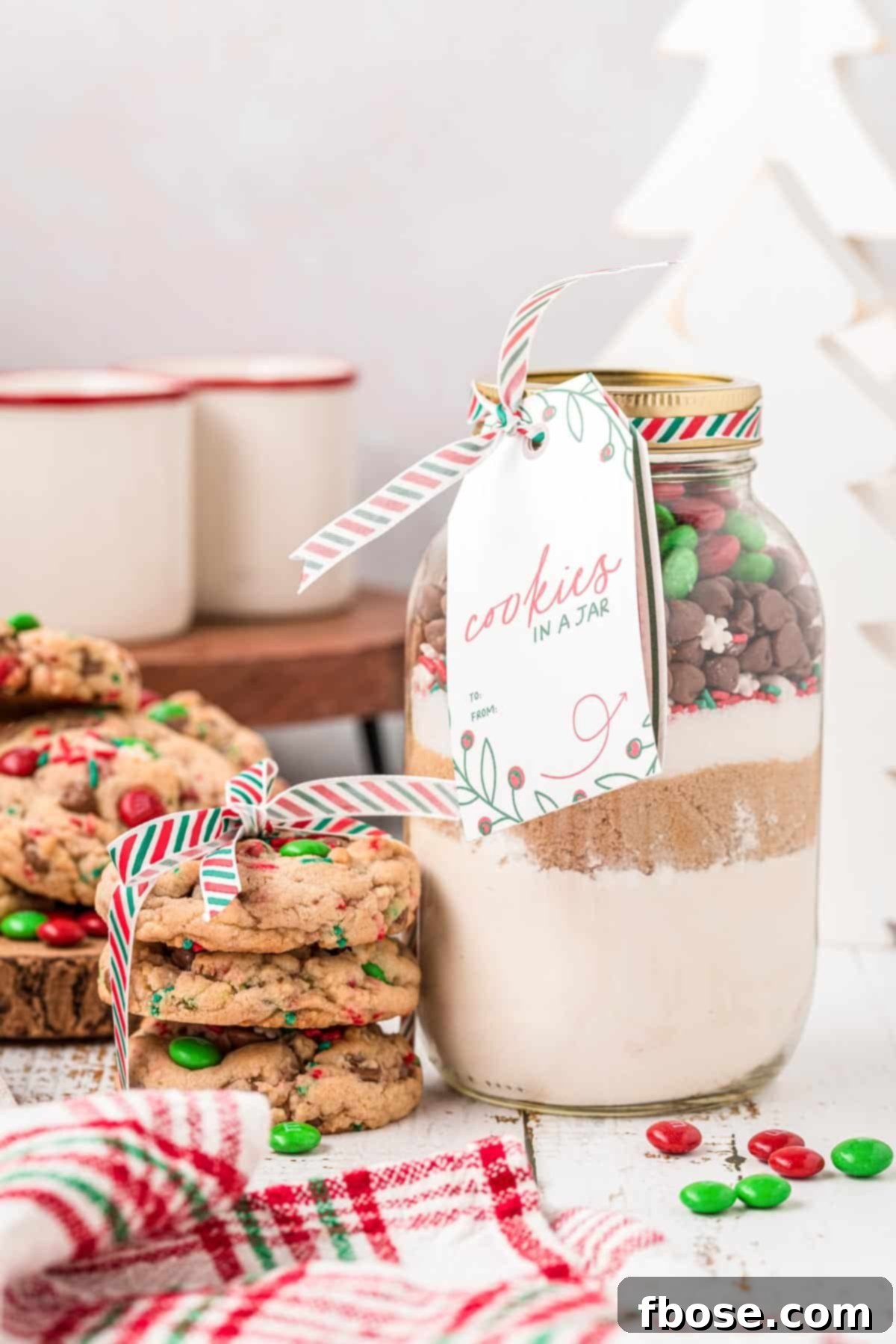 Holiday Cheer Cookie Jars 2 A jar of cookie mix with a stack of cookies next to it, showcasing the layers of ingredients.