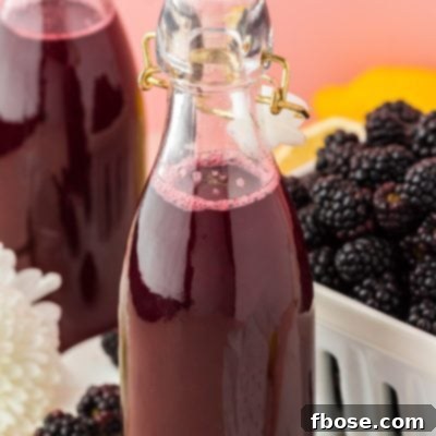 Close up of a bottle of homemade blackberry simple syrup, with another bottle and fresh berries in the background.