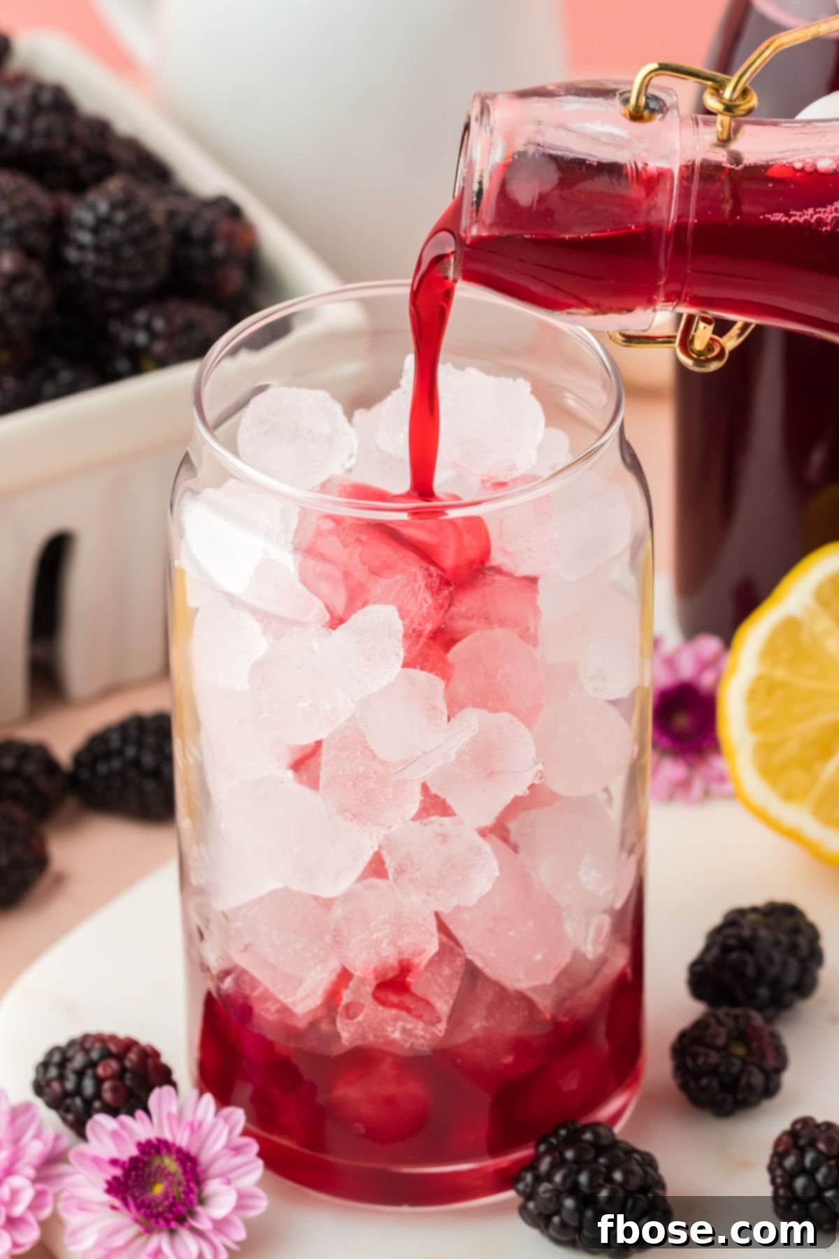 Homemade blackberry simple syrup being poured into a tall glass filled with ice, ready for a refreshing drink.