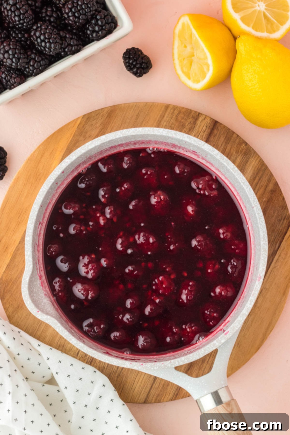 An overhead shot of a pot of blackberry simple syrup gently simmering on the stovetop, with the berries visibly breaking down and releasing their rich color into the liquid.