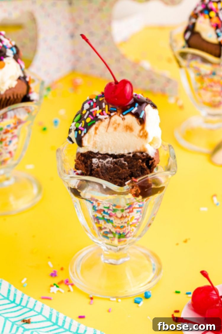A brownie cupcake with a bite taken out of it in a sundae dish with rainbow sprinkles.