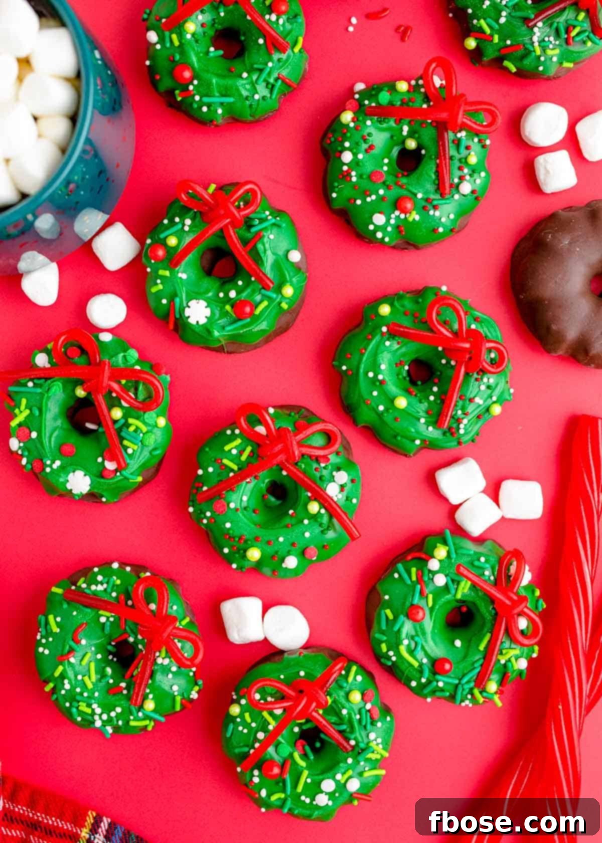 Simple Christmas Wreath Bites 3 Overhead photo of Christmas Wreath Cookies arranged on a festive red surface, highlighting their colorful sprinkles and Twizzler bows.