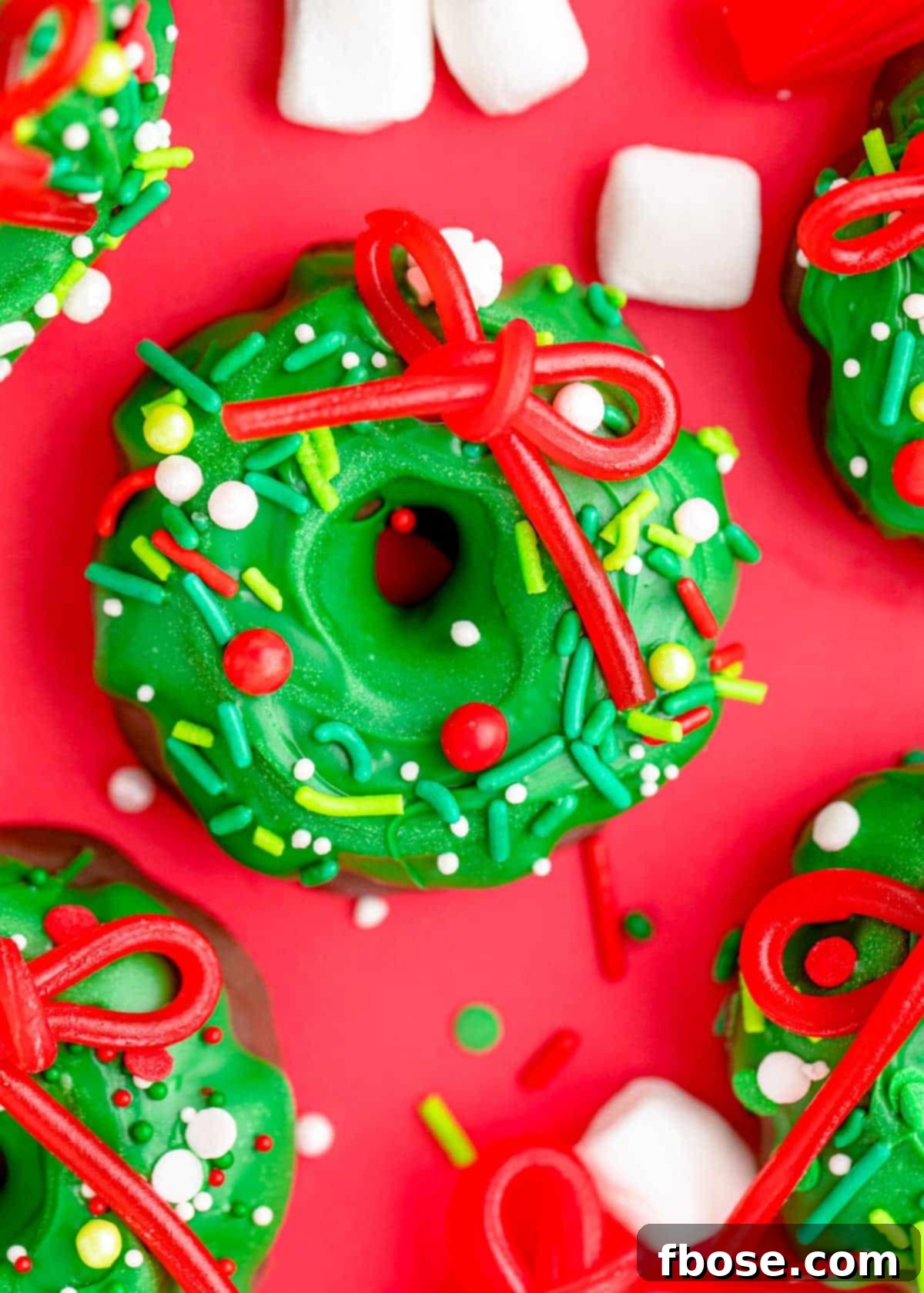 Simple Christmas Wreath Bites 5 A close-up shot of several Christmas wreath cookies on a vibrant red surface, highlighting their festive details.