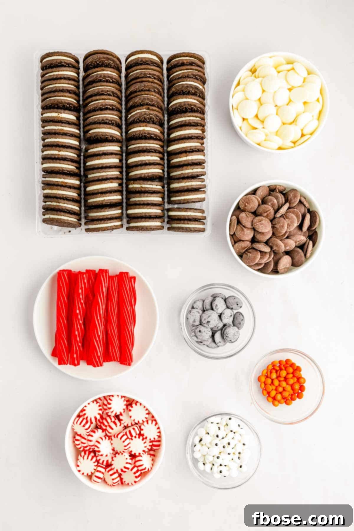Ingredients to make chocolate covered oreos decorated like penguins on a white surface.