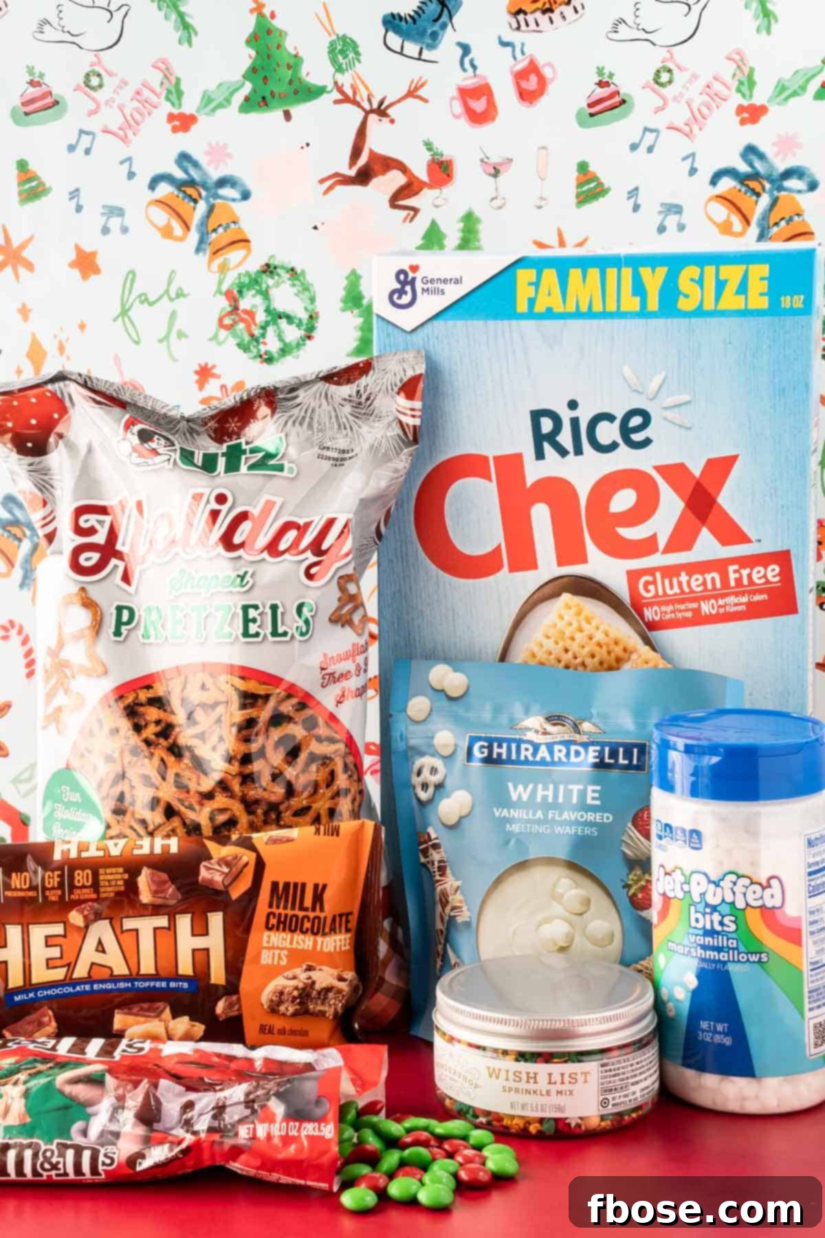 Ingredients to make Christmas Chex Snack Mix laid out on a red table.
