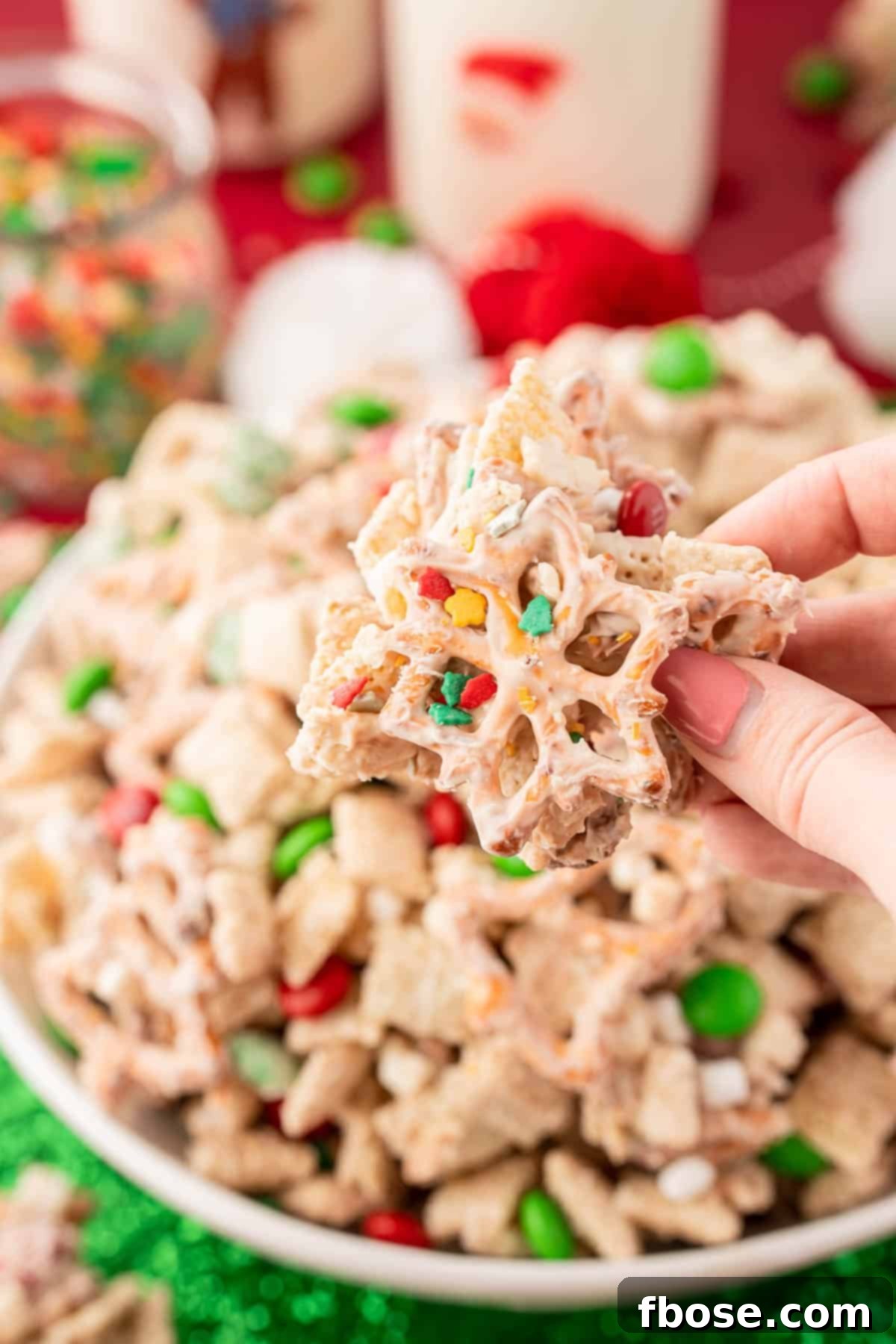 A woman's hand holding a clump of Christmas Chex Snack Mix to the camera, showcasing its texture.