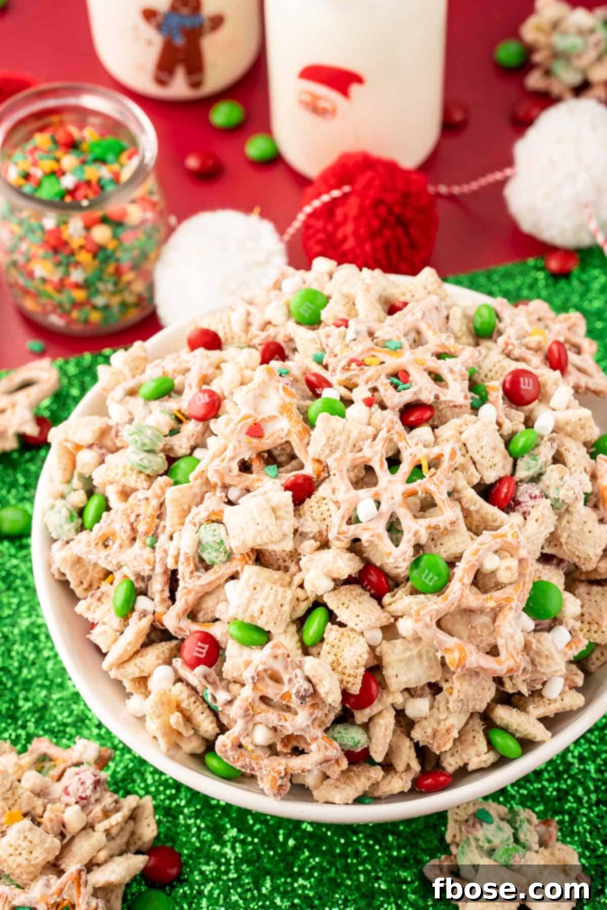 A bowl of Christmas Chex Mix on a green and red holiday decorated table, garnished with festive decor.