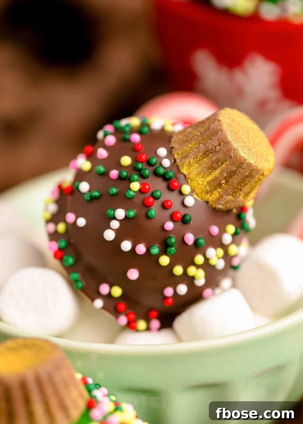 A chocolate covered oreo ball decorated like a Christmas Ornament in a small bowl of marshmallows.